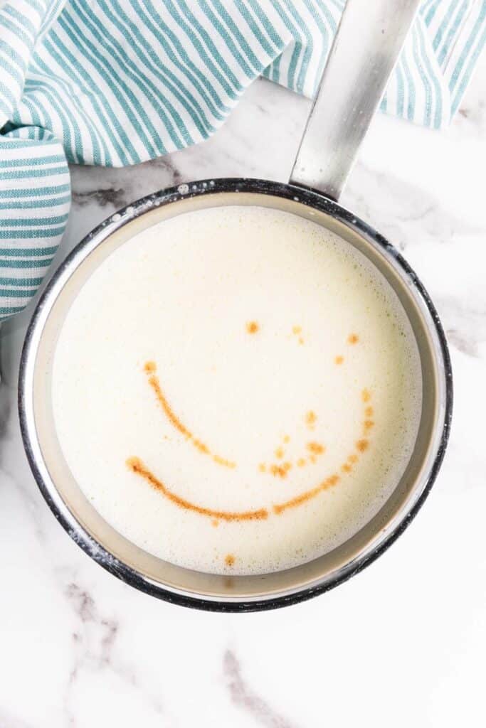 A saucepan of milk with cinnamon forming a smiley face pattern on the surface, perfect for crafting a creamy homemade eggnog.