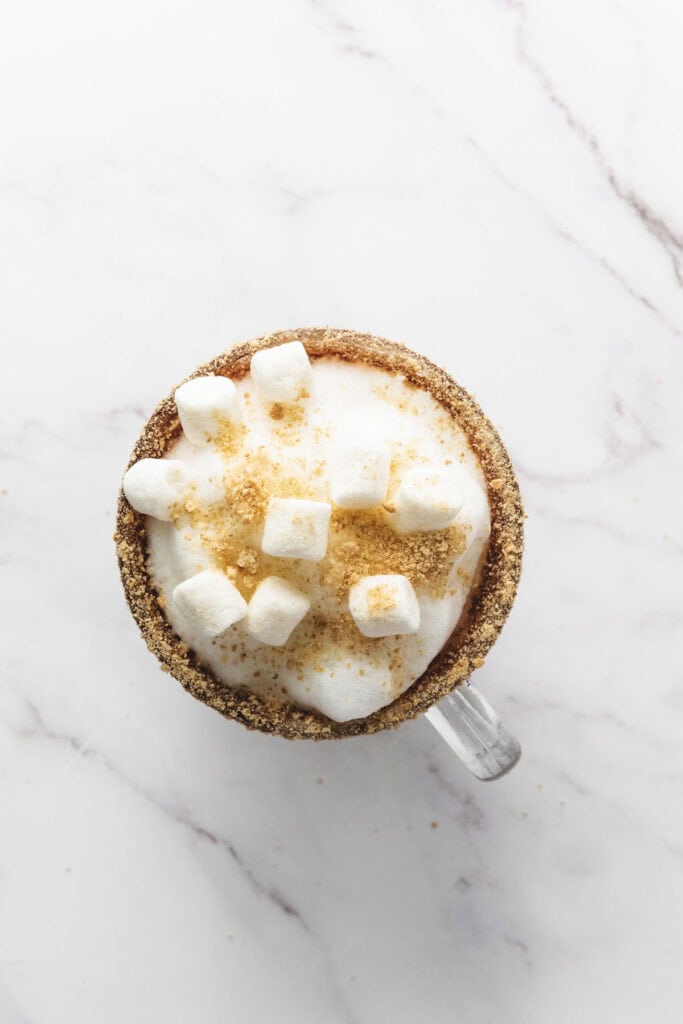 Overhead view of a mug filled with foamy S&rsquo;mores Latte topped with marshmallows and graham cracker crumbs.