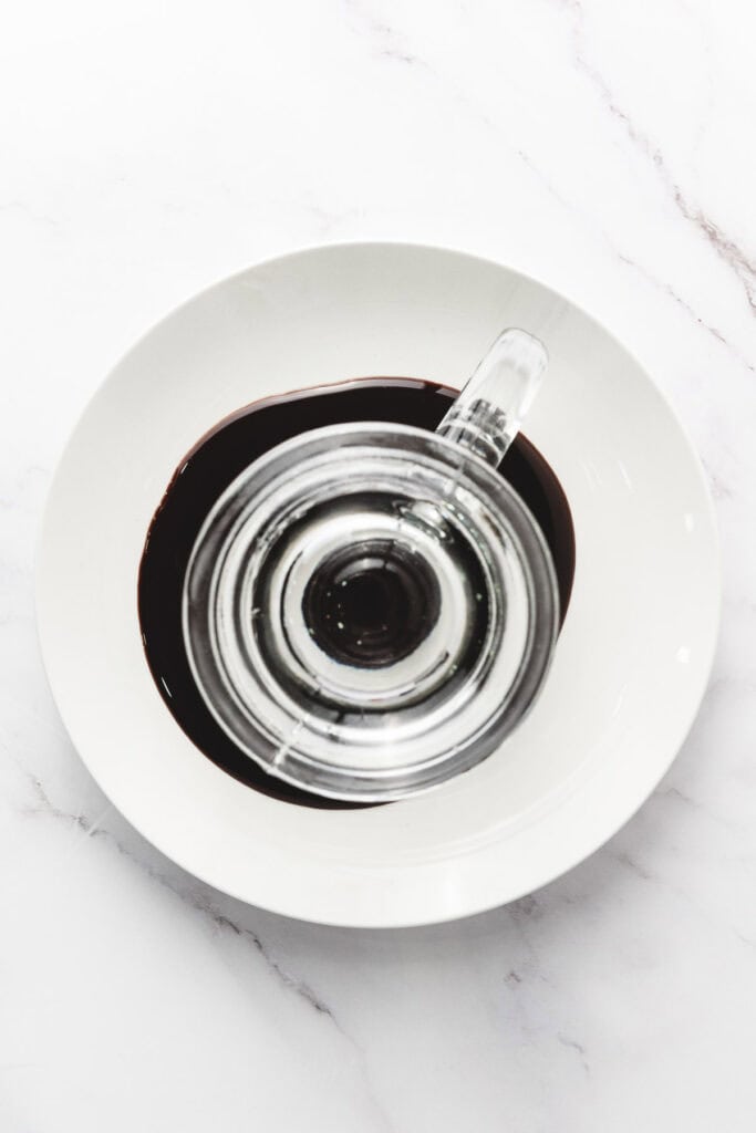 A glass pitcher sits in a white bowl with chocolate syrup around its base, viewed from above&mdash;perfect inspiration for your next S&rsquo;mores Latte Recipe.