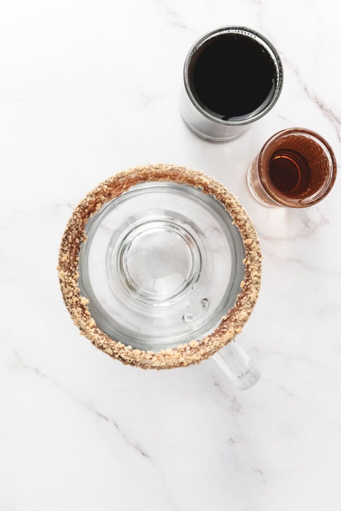 Overhead view of a glass rimmed with crushed nuts, beside glasses of dark soda and brown liquor&mdash;perfect inspiration for your next s&rsquo;mores latte or creative latte recipe.