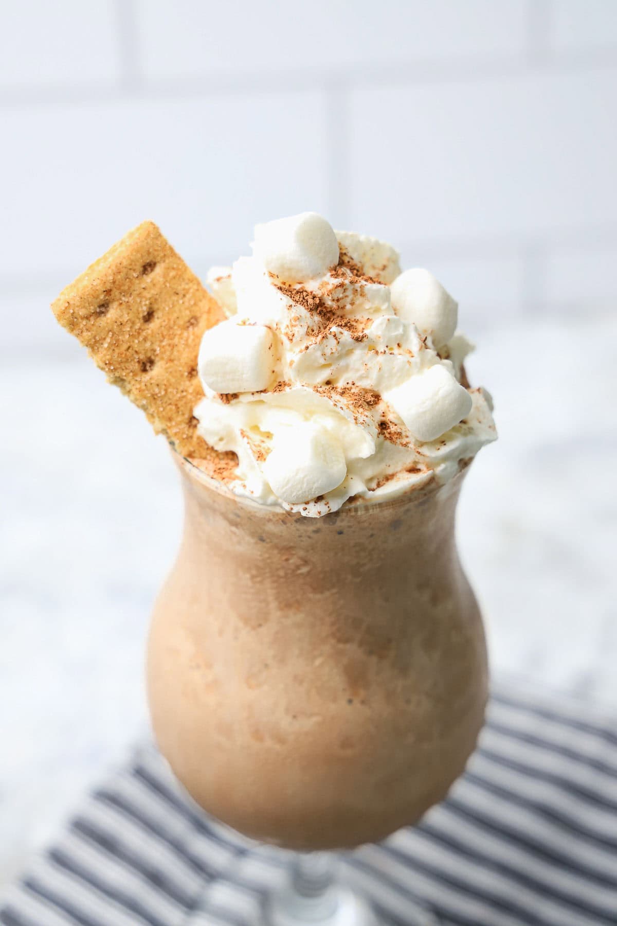 A s'mores milkshake topped with whipped cream, mini marshmallows, cocoa powder, and a graham cracker.