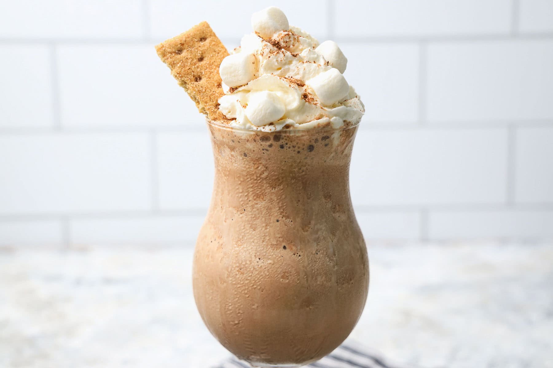 S'mores milkshake topped with whipped cream, mini marshmallows, cinnamon, and a graham cracker piece.