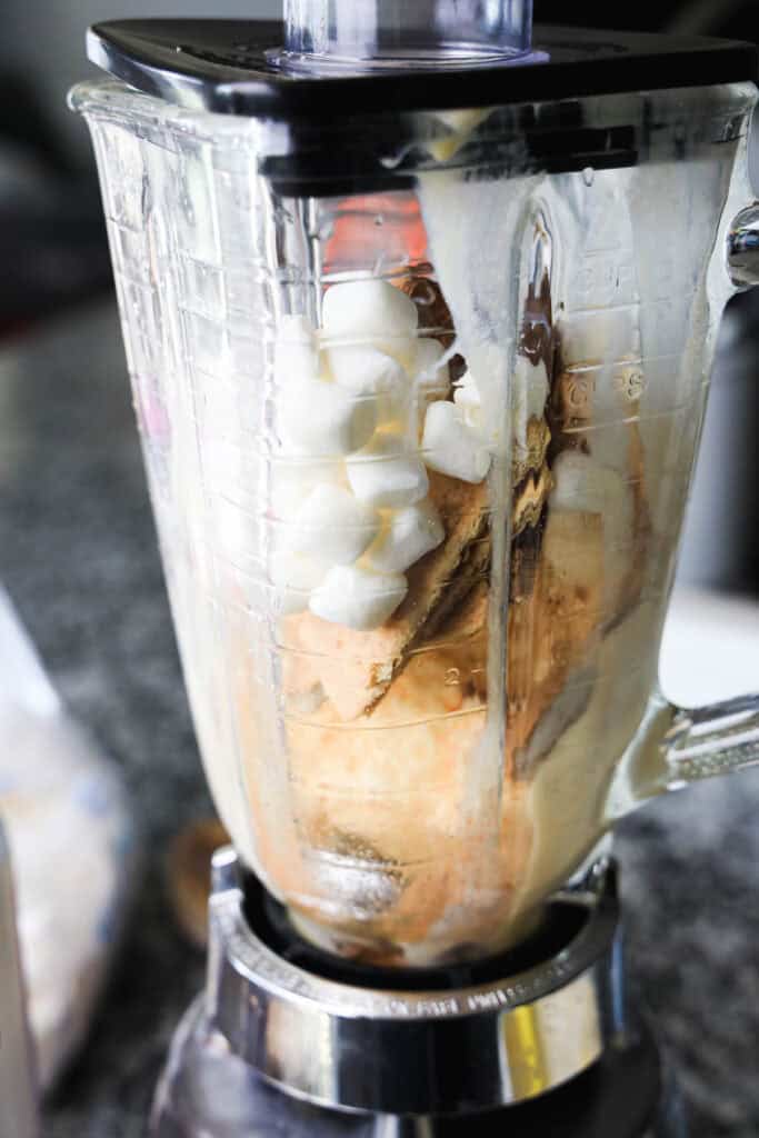 A blender filled with ice cream, marshmallows, and other ingredients, ready to be mixed into a delicious s'mores milkshake.