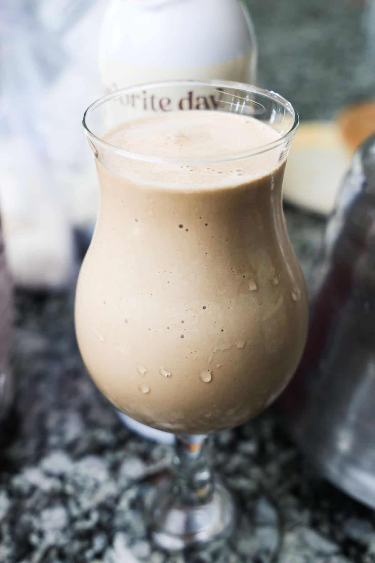 A creamy s'mores milkshake in a curvy glass, with condensation on the outside, sits invitingly on a granite countertop.