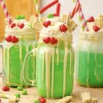 Green Grinch Freakshakes in jars topped with whipped cream, white chocolate, candy hearts, and straws&mdash;an irresistible Grinch recipe perfect for festive fun!.