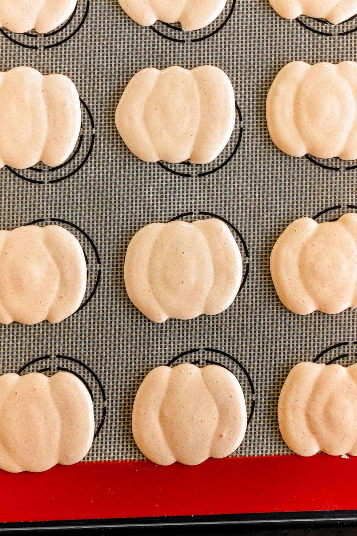 Pumpkin-shaped macaron shells on a baking mat, arranged in neat rows before being baked.