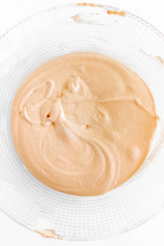 A glass bowl filled with smooth, light orange batter on a white surface.