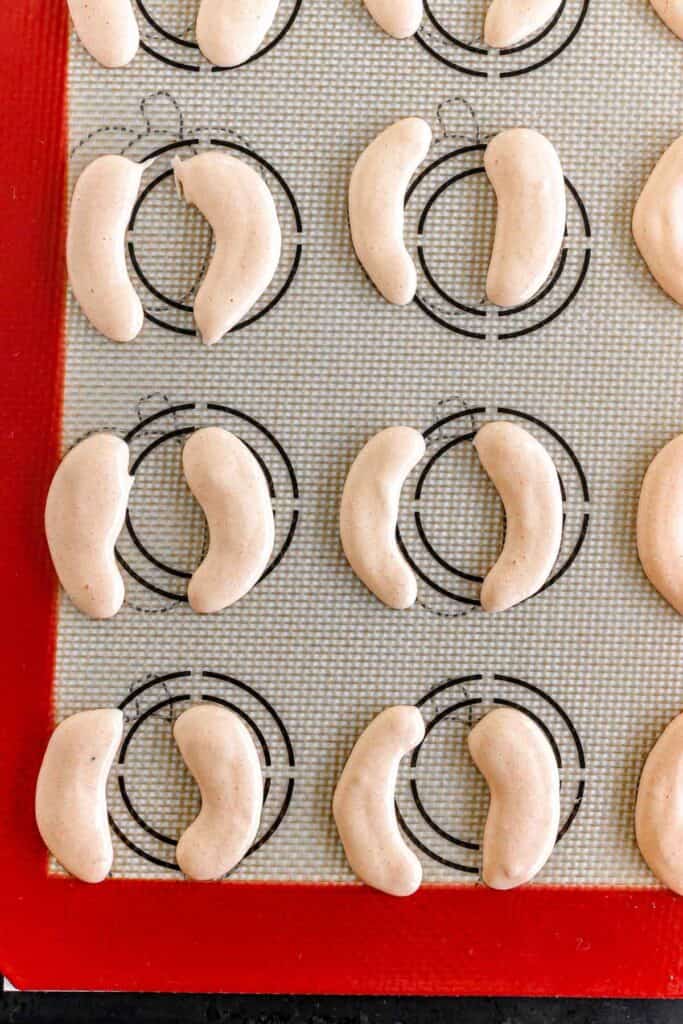Unbaked crescent-shaped cookies arranged on a silicone baking mat with circular guides.