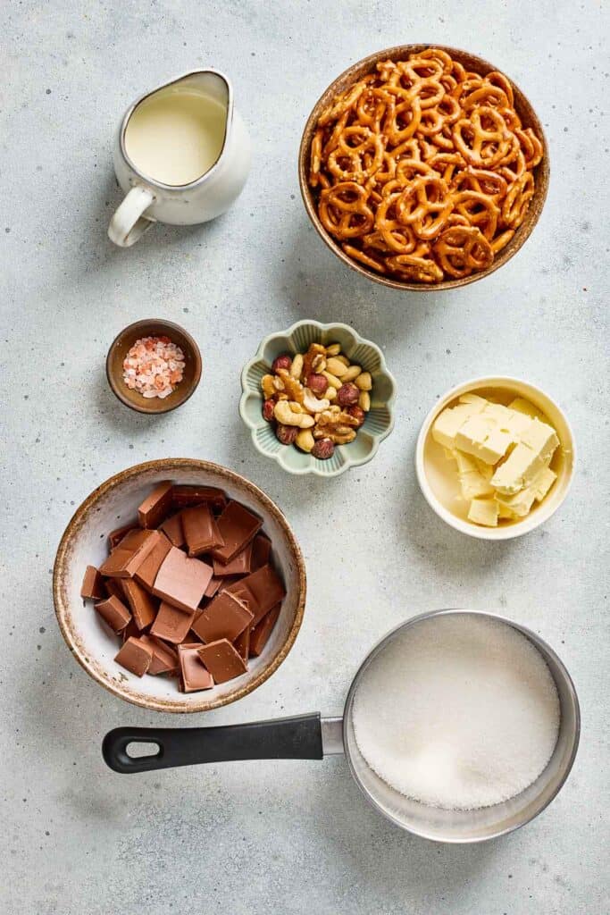 Top-down view of pretzels, mixed nuts, chocolate, butter, sugar, cream, and salt in separate bowls&mdash;perfect for making Salted Caramel Pretzel Bark.