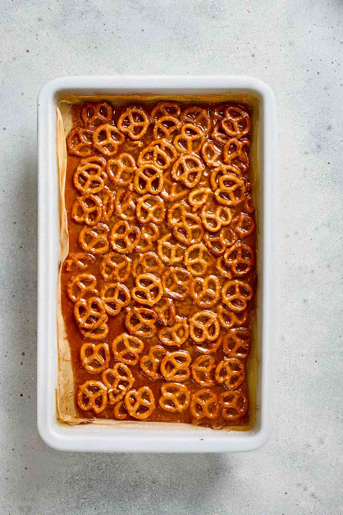 Rectangular dish with a baked dessert topped with Salted Caramel Pretzel bark, on a light-colored surface.