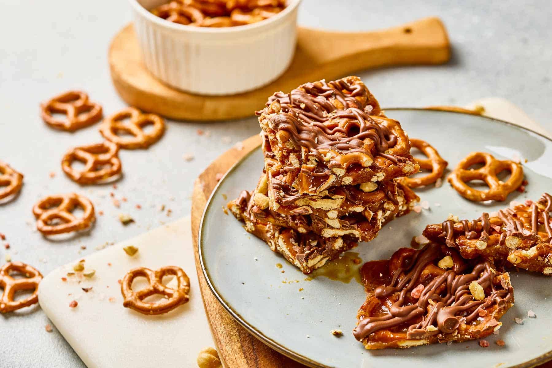 Three stacked pieces of salted caramel pretzel bark drizzled with chocolate, with pretzels scattered on the table.