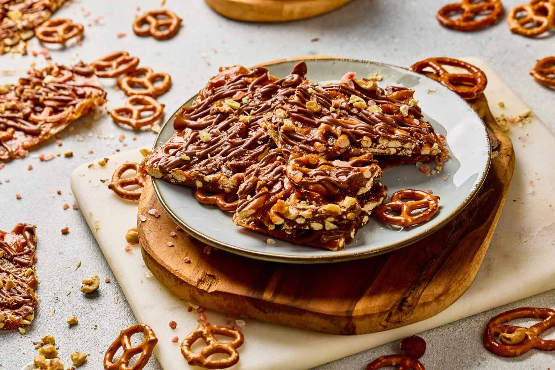 A plate of chocolate-drizzled Pretzel Bark with scattered pretzels and bark pieces on the table, featuring hints of salted caramel for a sweet and salty treat.