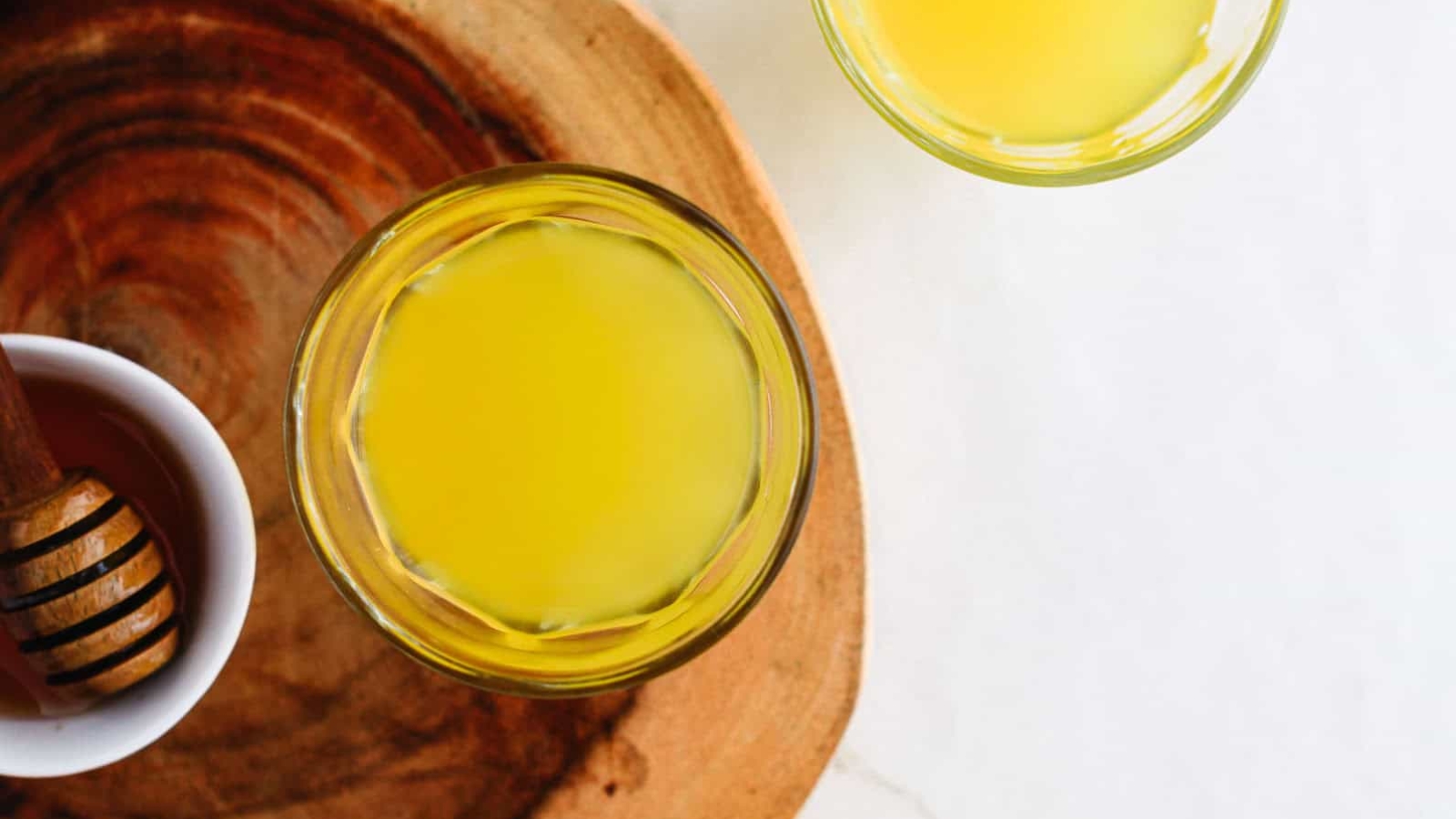Two glasses of yellow juice on a wooden tray, with a bowl of honey and dipper nearby.