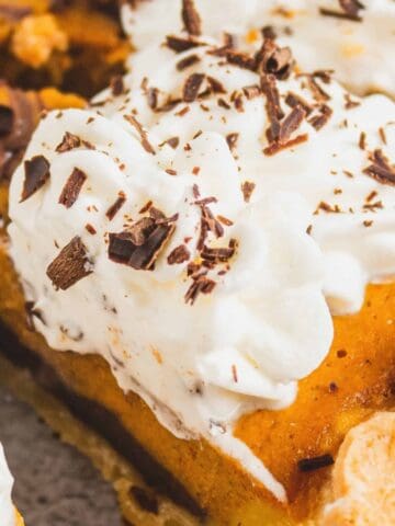 Slice of pumpkin pie topped with whipped cream and chocolate shavings on a pie plate.