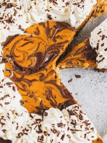Pumpkin pie with whipped cream and chocolate shavings, one slice missing, in a glass pie dish.