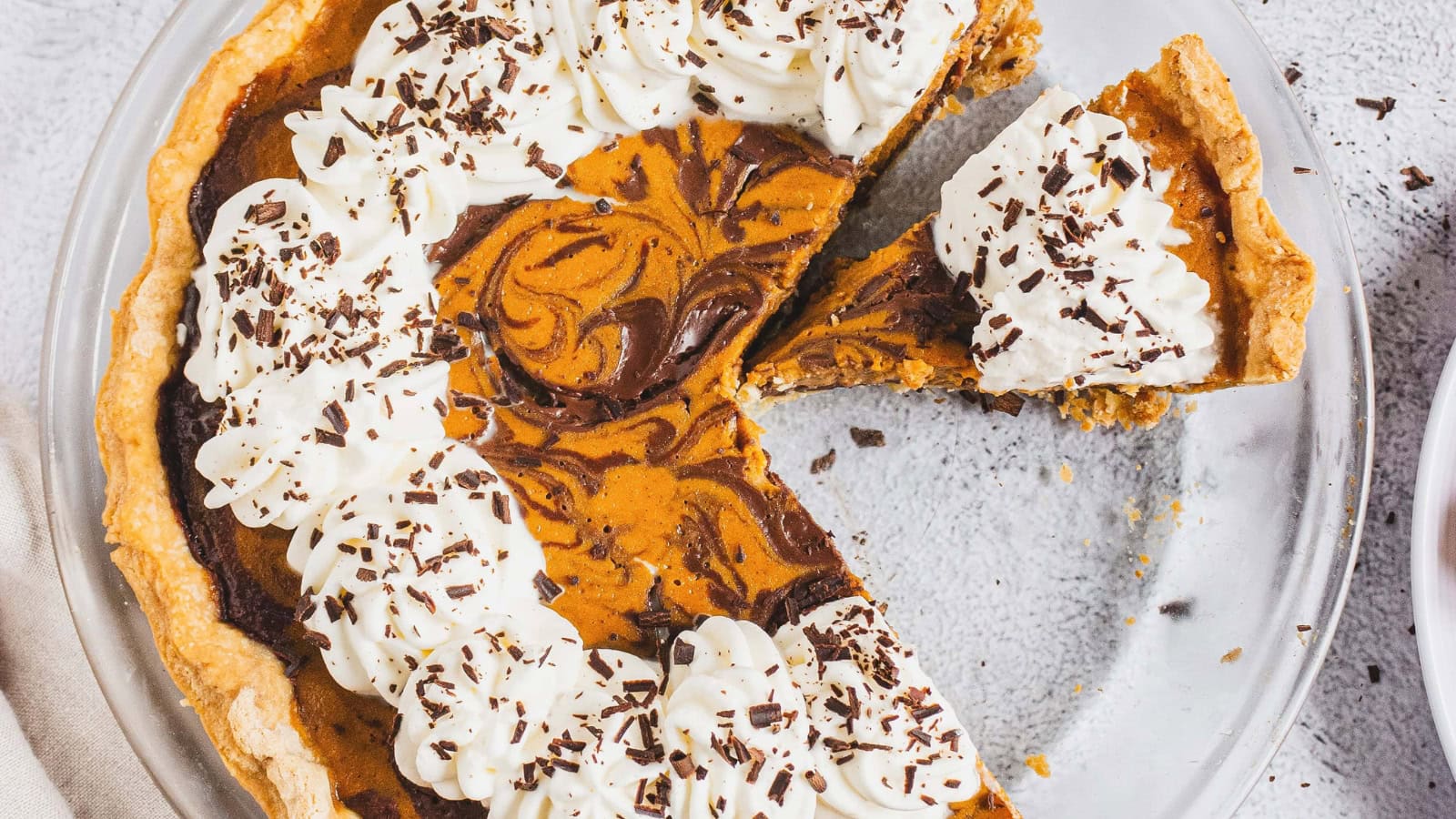 Close-up of pumpkin pie slices topped with whipped cream and chocolate shavings in a pie dish.