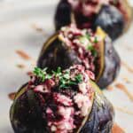 Close-up of goat cheese stuffed figs with fresh herbs, drizzled with honey, on a white plate.