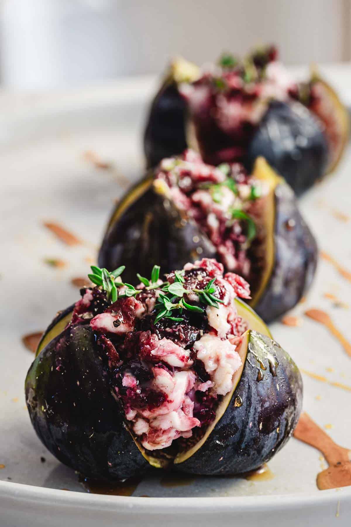 Close-up of goat cheese stuffed figs with fresh herbs, drizzled with honey, on a white plate.