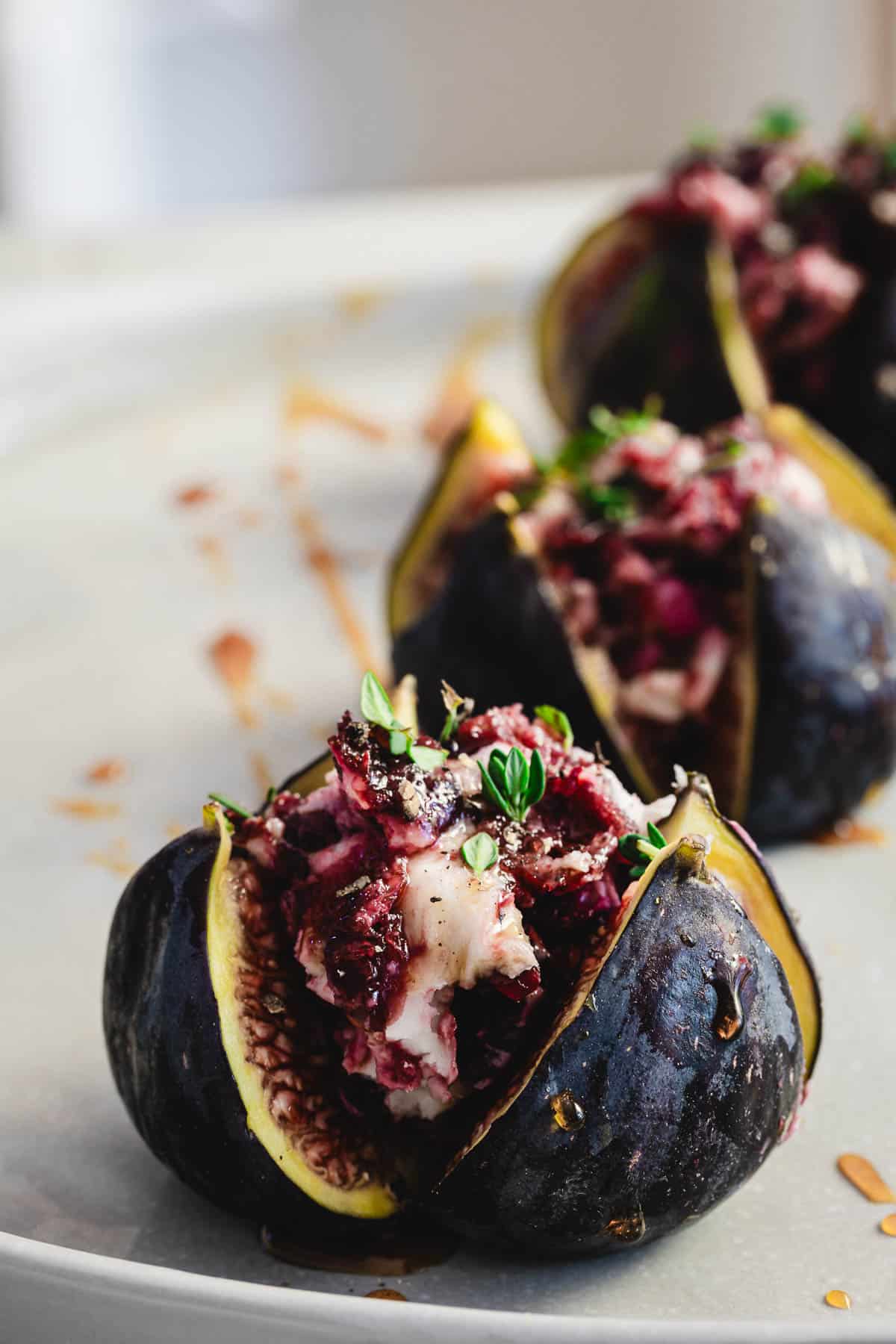 Close-up of goat cheese stuffed figs with herbs and a berry mixture, garnished with fresh thyme.