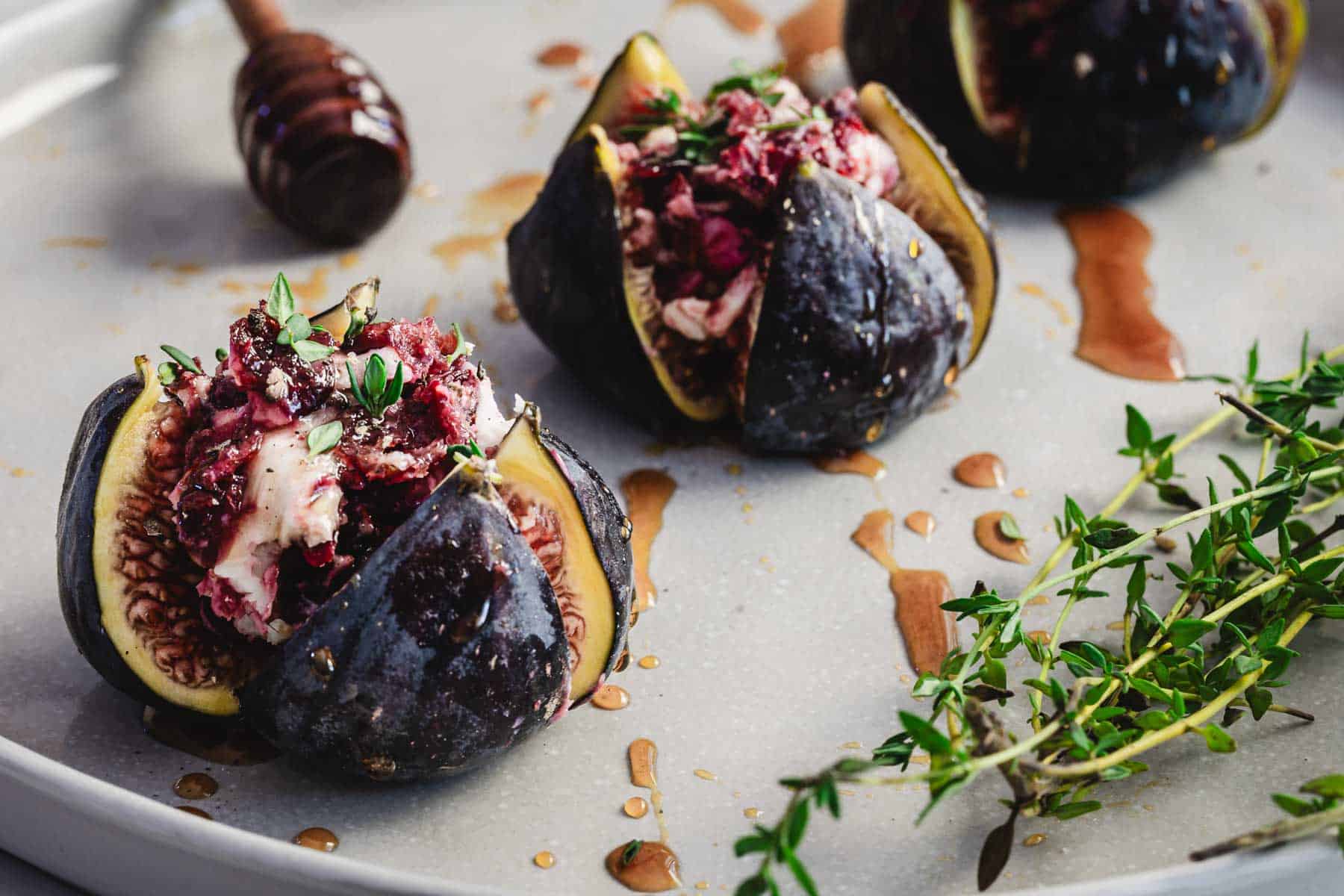 Goat cheese stuffed figs with herbs, drizzled in honey, are served on a plate garnished with fresh thyme sprigs.