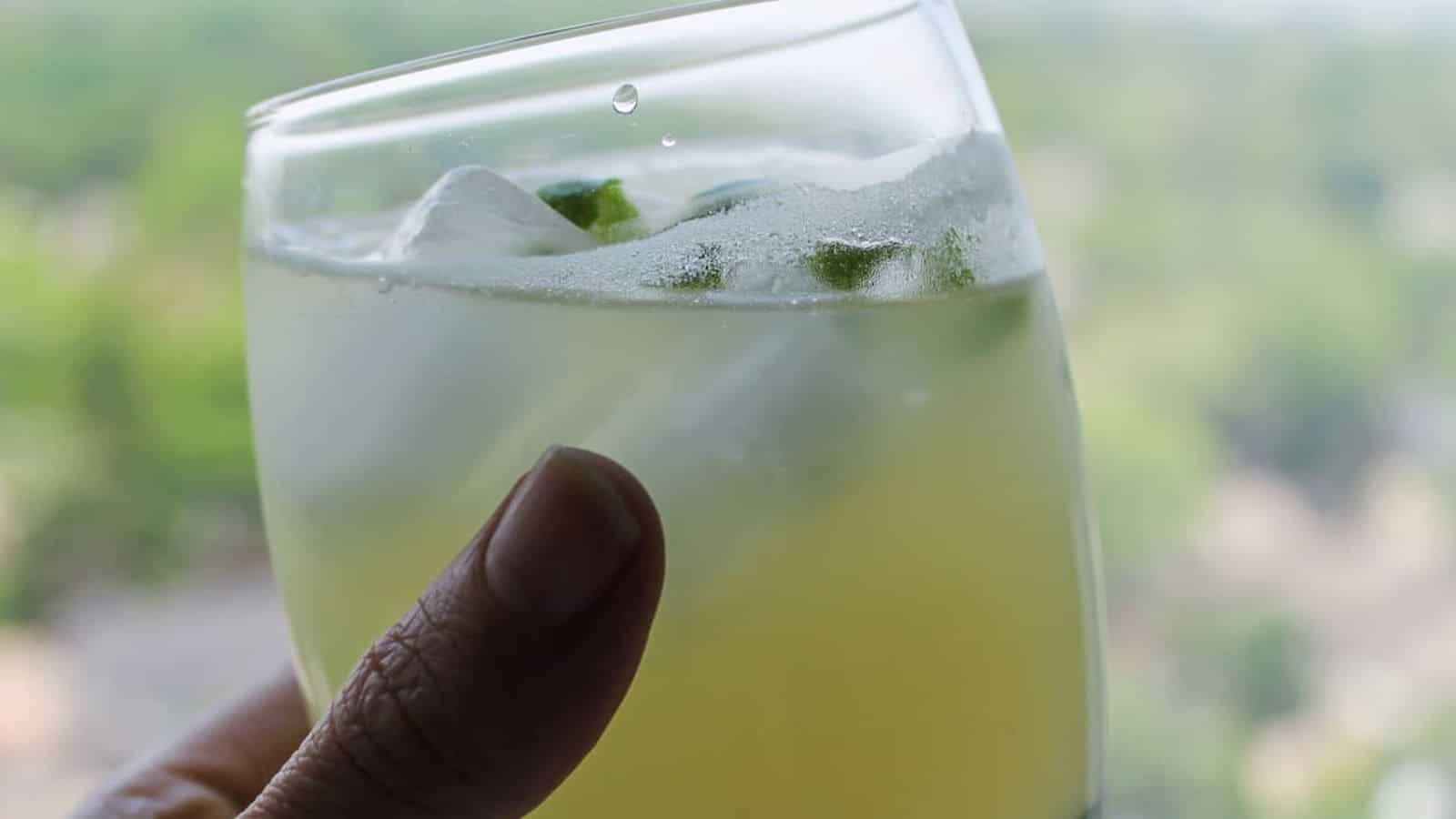 A hand holding a glass of green apple juice.