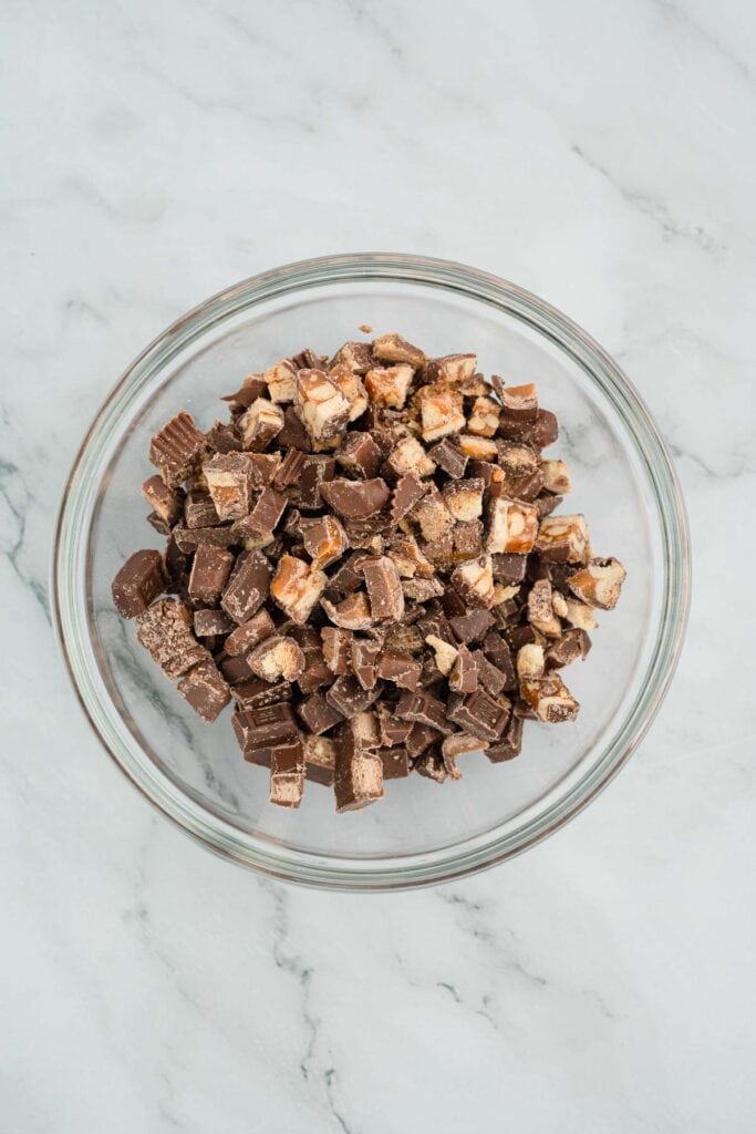 A glass bowl filled with chopped chocolate candy bars on a marble surface.