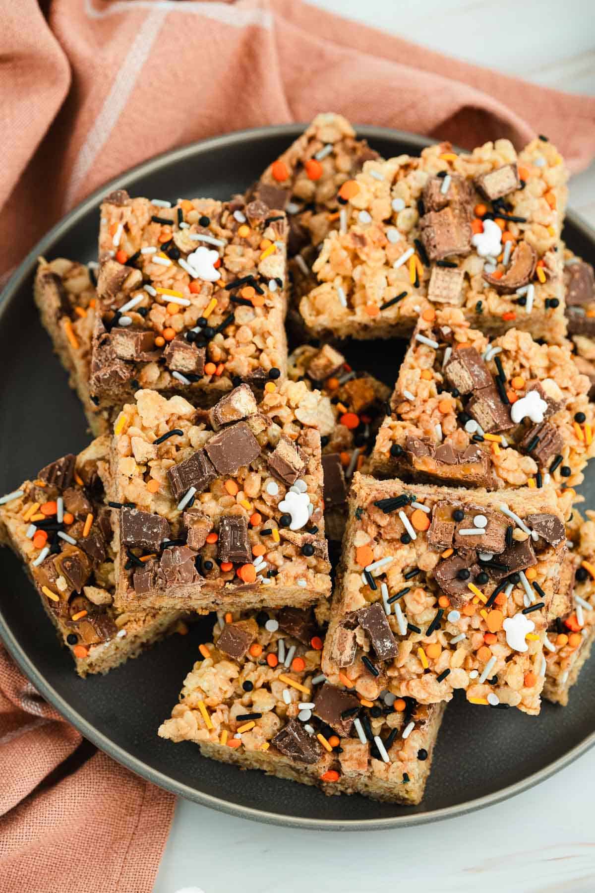 A plate of decorated Rice Krispies treats topped with chocolate chunks and colorful sprinkles.