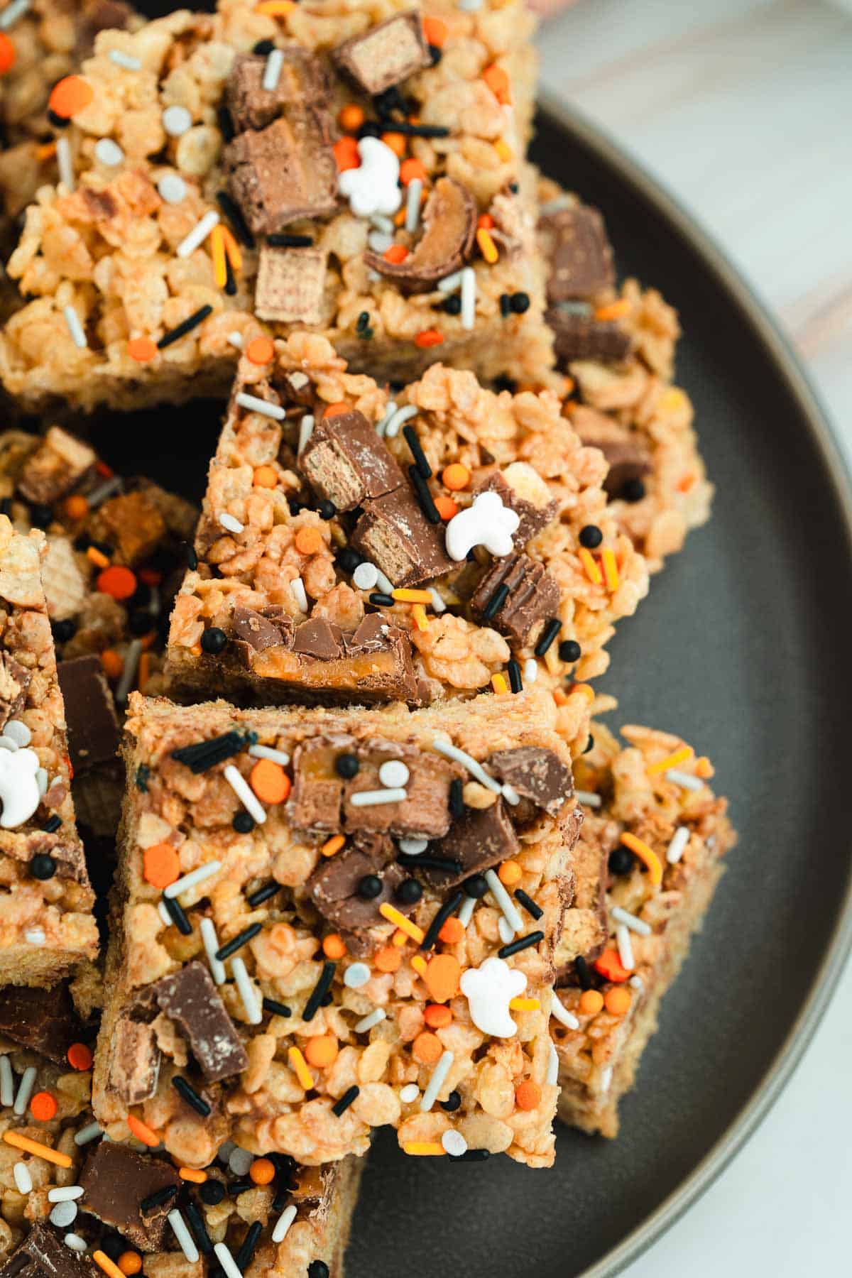 Close-up of rice crispy treats topped with chocolate pieces and orange, white, and black sprinkles on a plate.