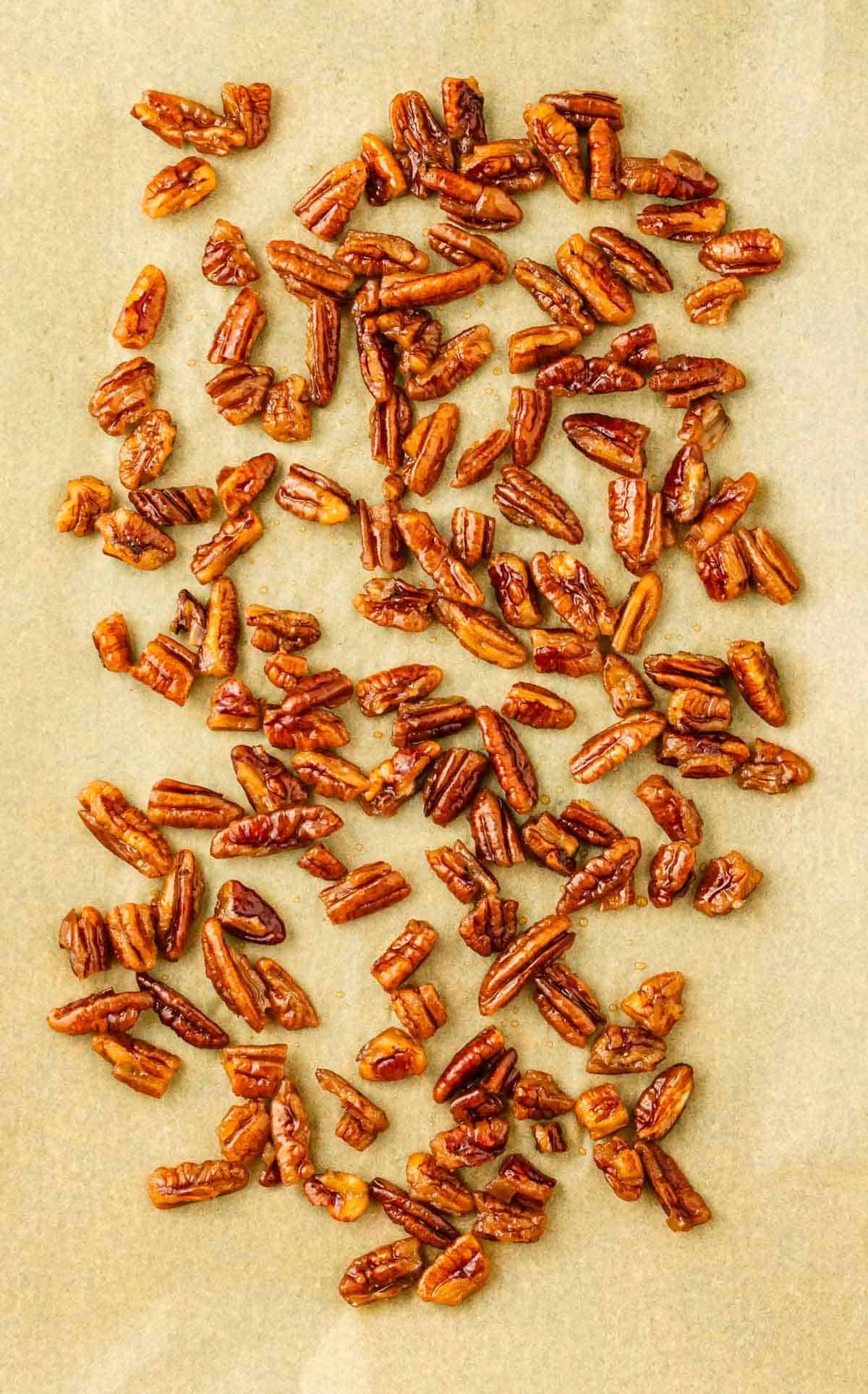 Sweet Toasted Pecans halves are scattered on a sheet of brown parchment paper, perfect for any homemade recipe.