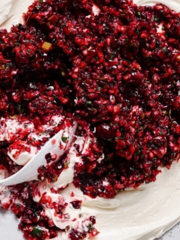A creamy white dip topped with a chunky cranberry salsa, being scooped with a spoon.