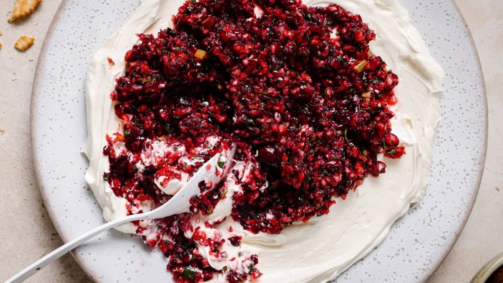 A cracker being dipped into a dish of jalape&ntilde;o cranberry dip.