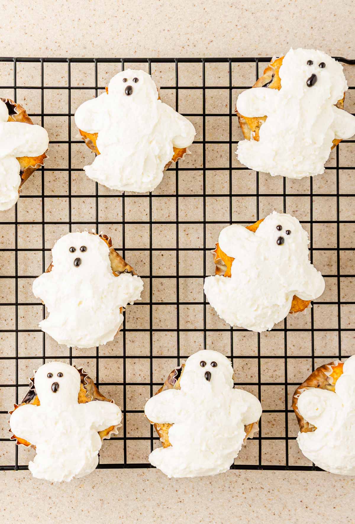 Ghost-shaped cookies with white frosting and BOO-berry black eyes on a cooling rack, topped with spooky SCREAM Cheese Icing for a hauntingly sweet treat.