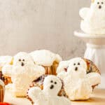 Ghost Muffins decorated to look like white ghosts with Scream Cheese Icing and black eyes, arranged on a wooden board and cake stand.