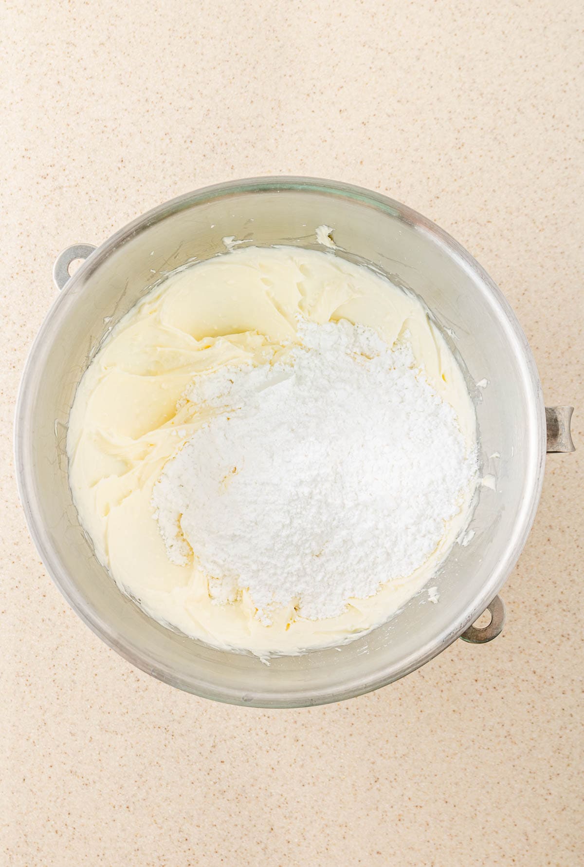 A metal bowl with creamed butter and powdered sugar sits on a light countertop, ready to be mixed into SCREAM Cheese Icing for your Ghost Muffins.