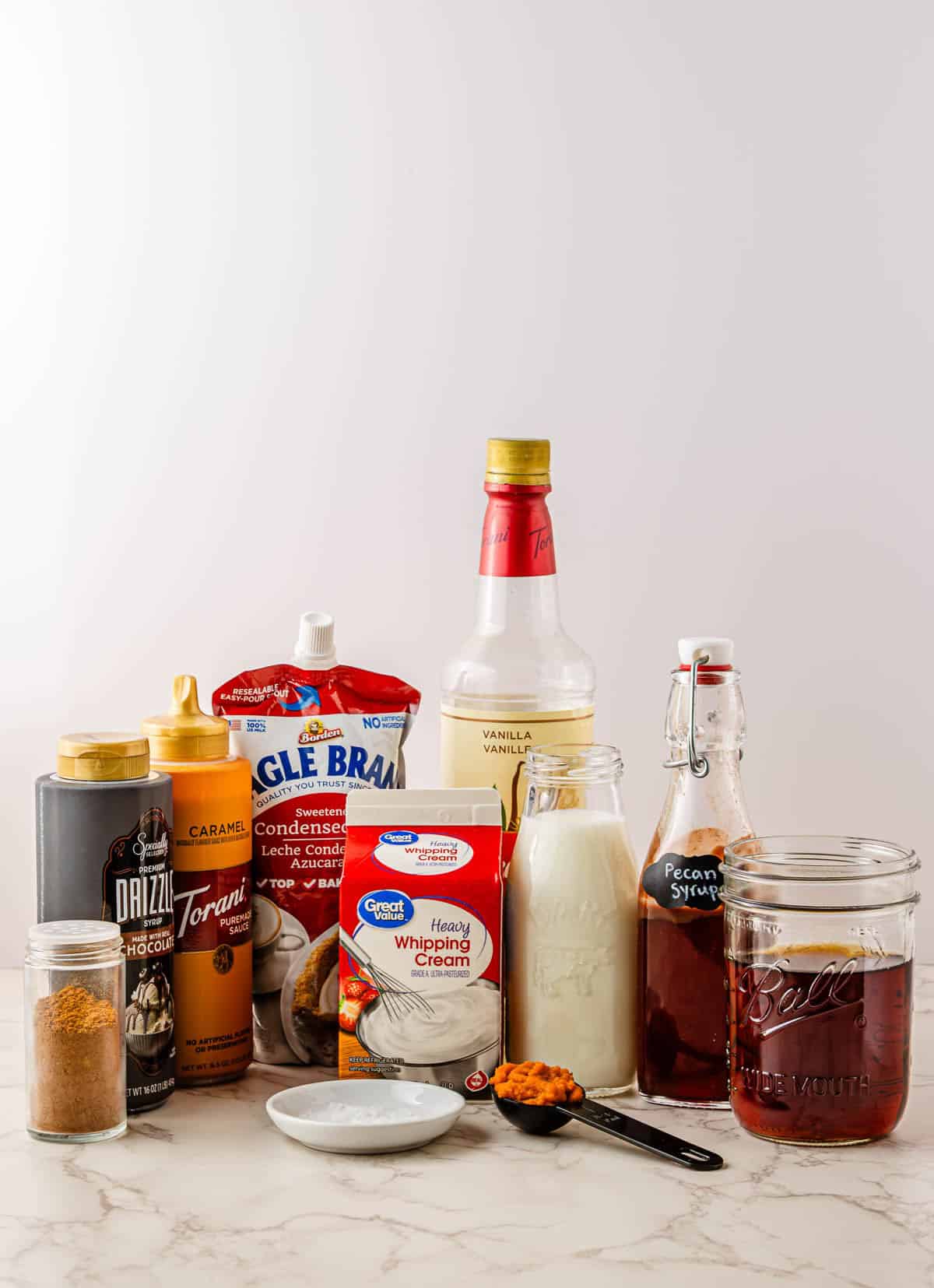 Various ingredients for a recipe, including milk, cream, syrups, condensed milk, and spices on a counter&mdash;perfect for making a Starbucks Copycat Pumpkin Cream Cold Brew at home.