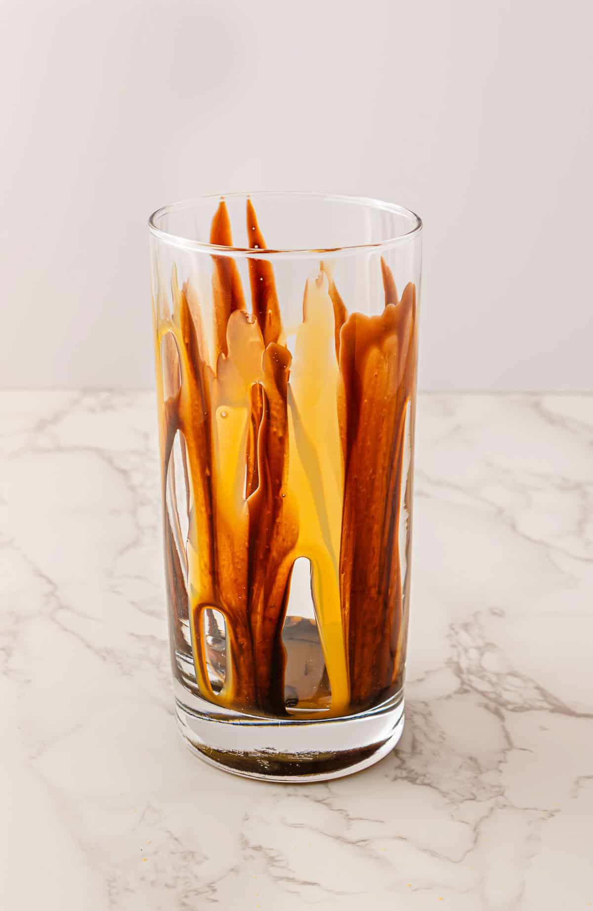 A glass with chocolate and caramel sauces drizzled inside, reminiscent of a decadent Caramel Turtle treat, sits on a marble surface.