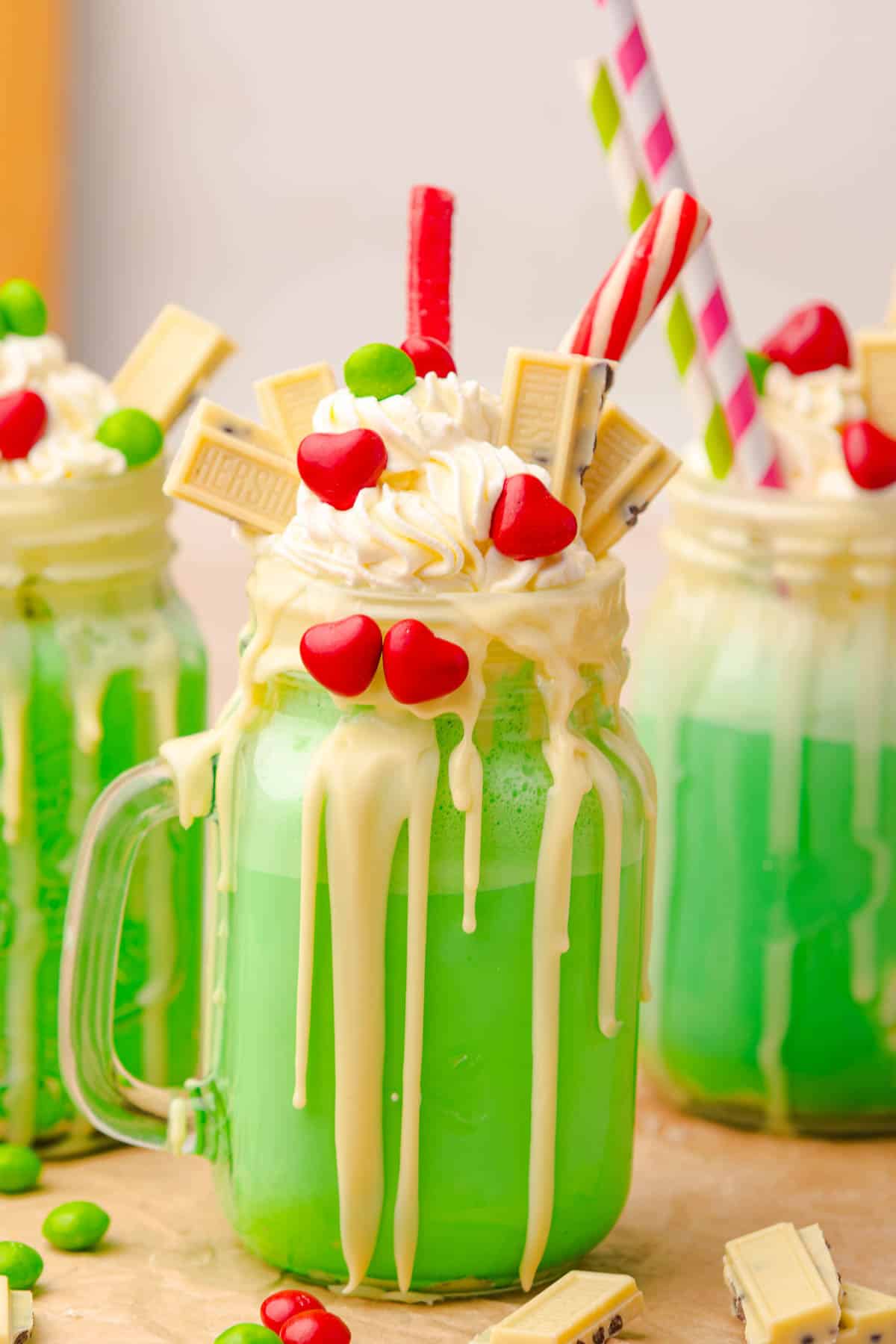 Green Grinch Freakshake in a jar, topped with whipped cream, candy, white chocolate, and festive red and green decorations&mdash;perfect for your next holiday freakshake recipe!.