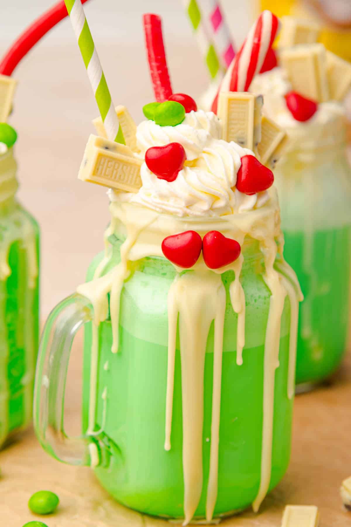 A green Grinch Freakshake in a mason jar, topped with whipped cream, white chocolate, and red heart candies.
