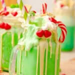 A green Grinch Freakshake in a glass jar, topped with whipped cream, candy, and a striped straw.