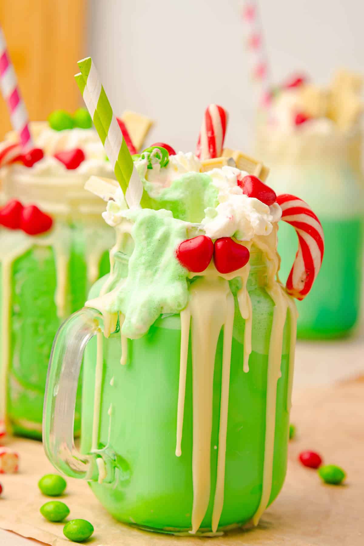 A green Grinch Freakshake in a glass jar, topped with whipped cream, candy, and a striped straw.