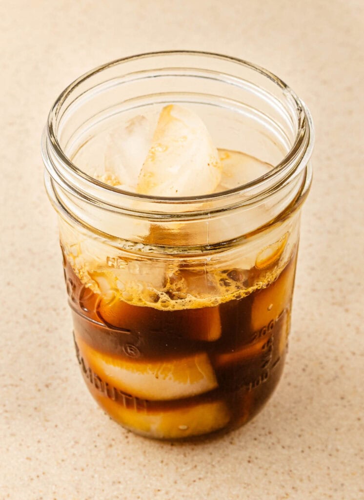 A mason jar filled with iced coffee and large ice cubes&mdash;an irresistible Starbucks Copycat Oatmilk Shaken Espresso&mdash;sits on a light speckled countertop.