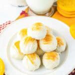 A plate of white chocolate-covered Snickerdoodle Truffles topped with yellow sprinkles sits beside a glass of milk, perfect for anyone craving a delicious twist on the classic truffles recipe.
