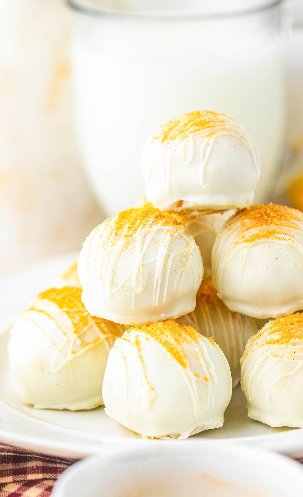 A stack of white chocolate Snickerdoodle truffles with yellow sprinkles, drizzled with white chocolate on a white plate.