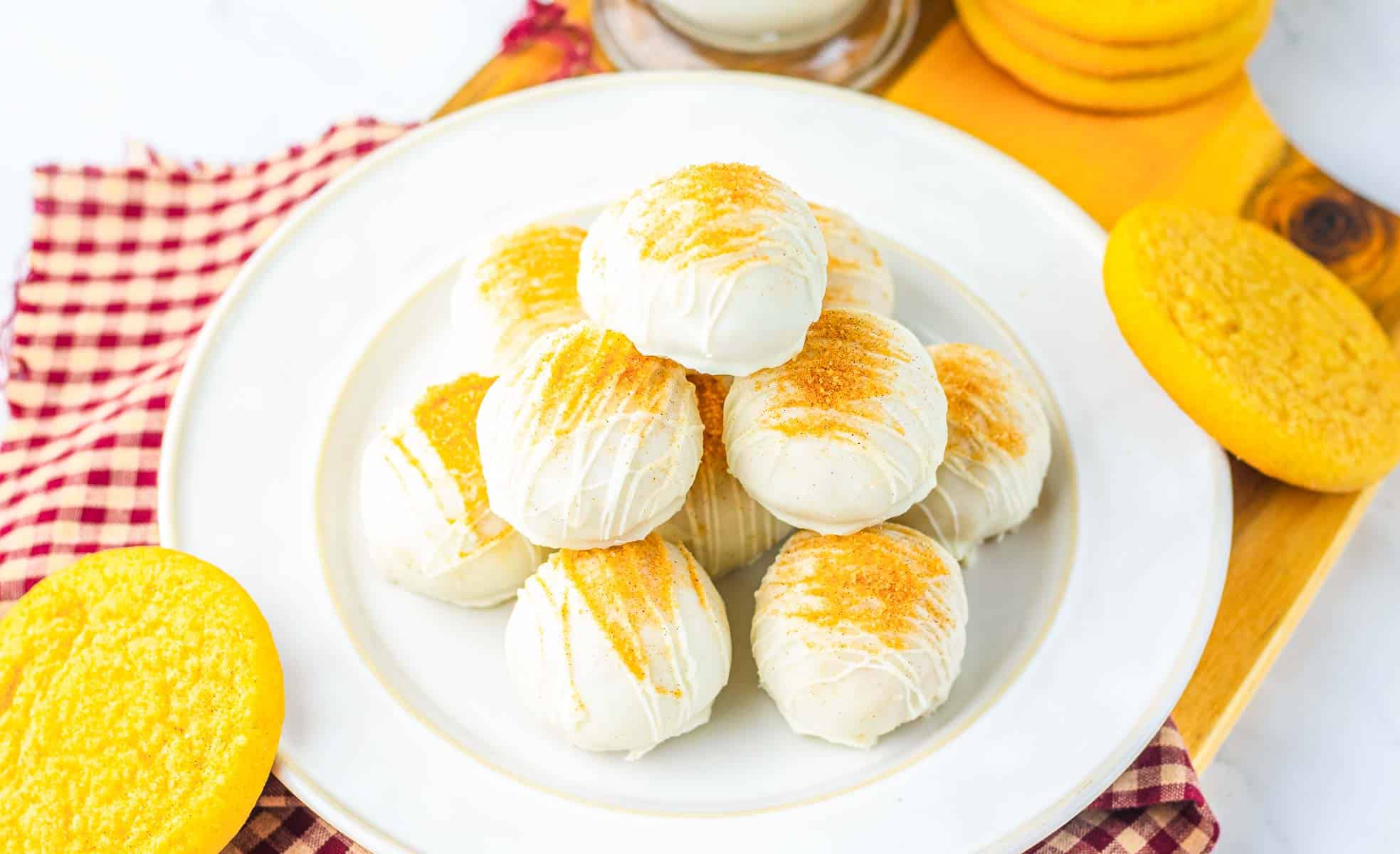 A plate of white chocolate-covered snickerdoodle cookies topped with golden crumbs, surrounded by yellow cookies&mdash;a delightful recipe for any occasion.