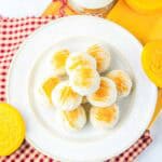 A plate of round, white snickerdoodle cookies with yellow sugar, next to milk and yellow cookies on a gingham cloth—a delightful recipe for any occasion.