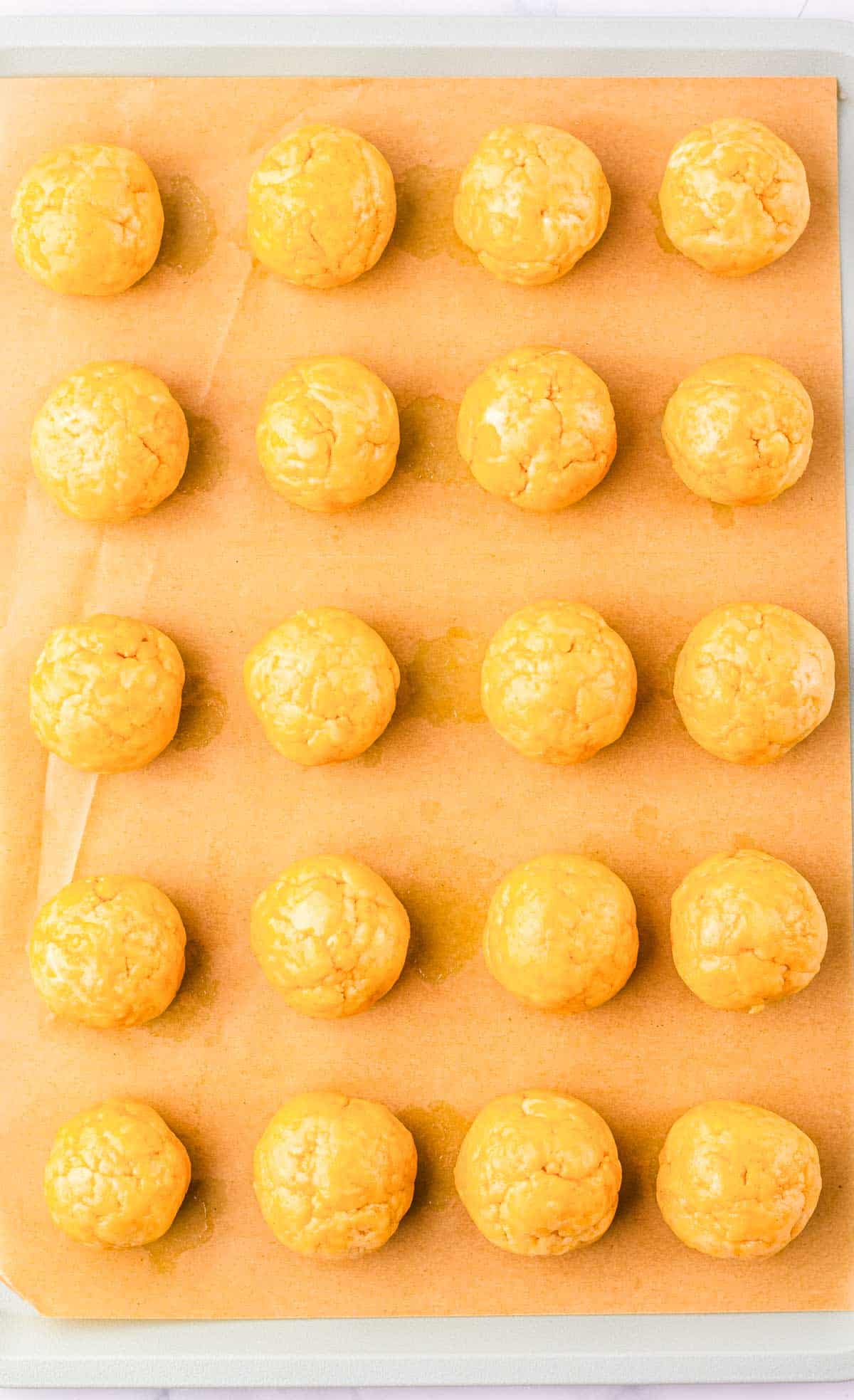 Twenty unbaked Snickerdoodle dough balls arranged in rows on a baking sheet lined with parchment paper, ready to complete this delicious recipe.
