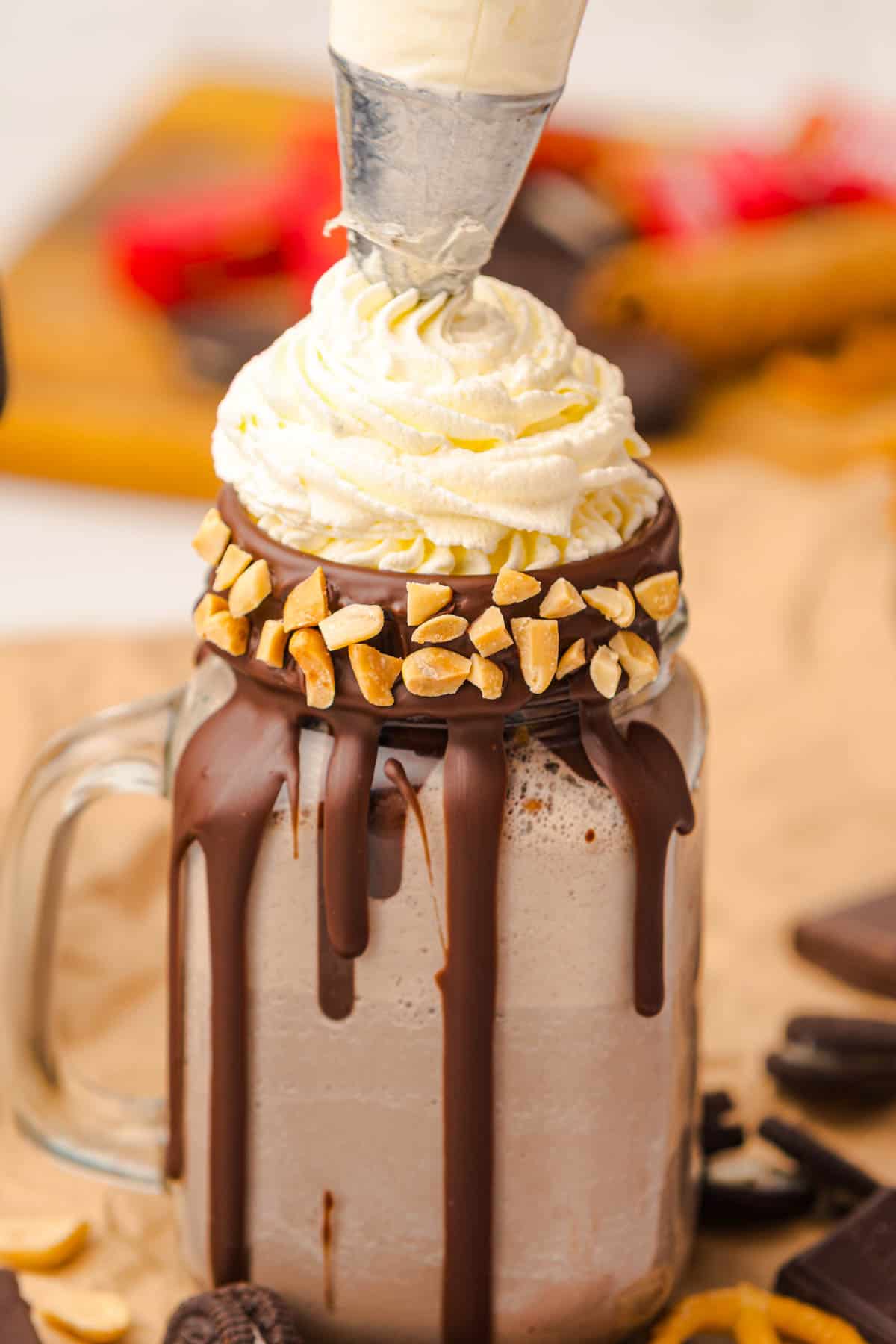 A mason jar with a rich Chocolate Freakshake, topped with whipped cream, chopped nuts, and a generous chocolate drizzle on the rim.
