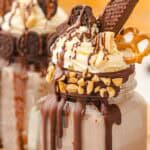 A mason jar chocolate freakshake topped with whipped cream, chocolate, cookies, pretzel, wafer, and chopped nuts. Try this freakshake recipe for the ultimate indulgent treat!.