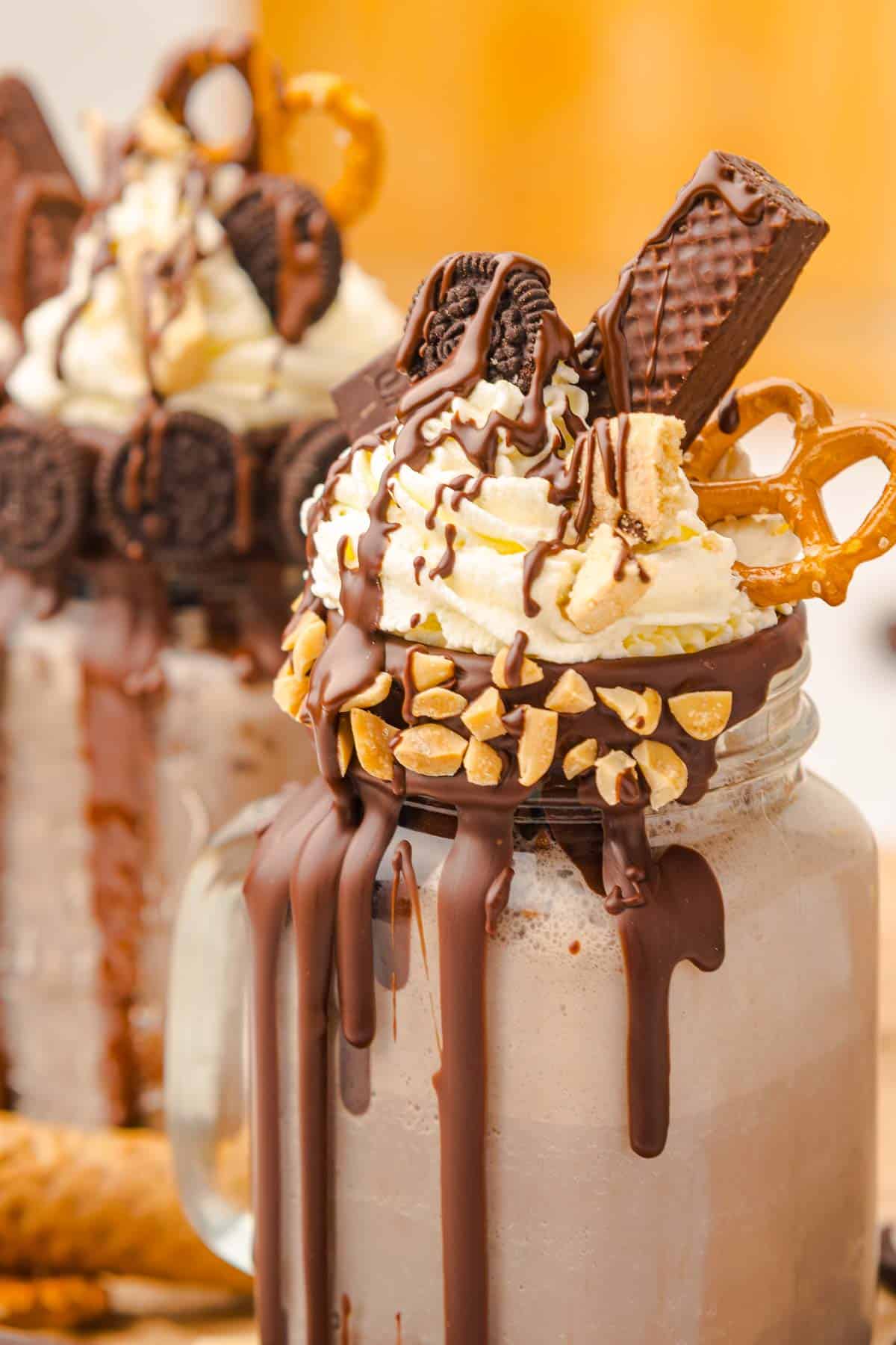 A mason jar chocolate freakshake topped with whipped cream, chocolate, cookies, pretzel, wafer, and chopped nuts. Try this freakshake recipe for the ultimate indulgent treat!.