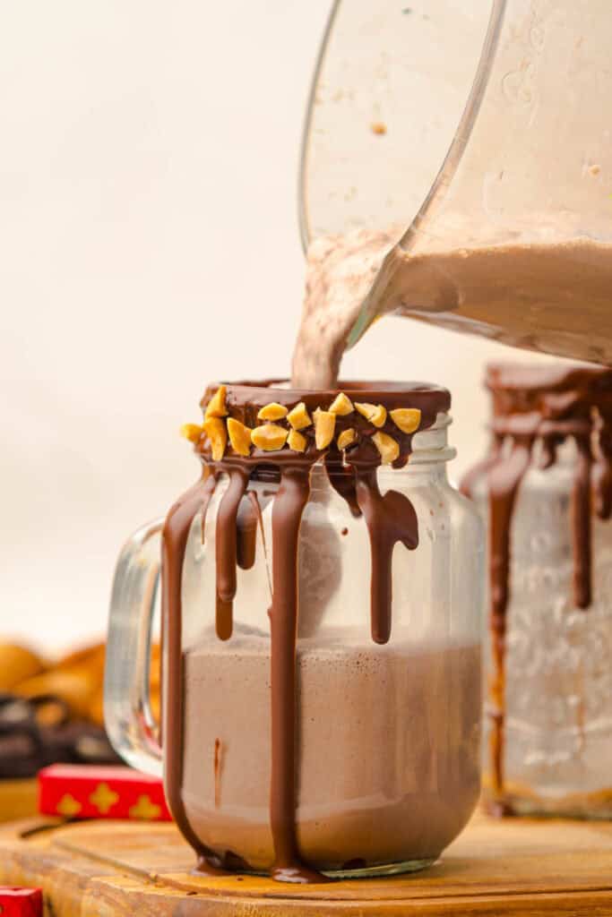 A rich chocolate milkshake is poured into a mason jar, with chocolate and chopped peanuts lining the rim&mdash;a perfect Chocolate Freakshake Recipe for indulgent moments.